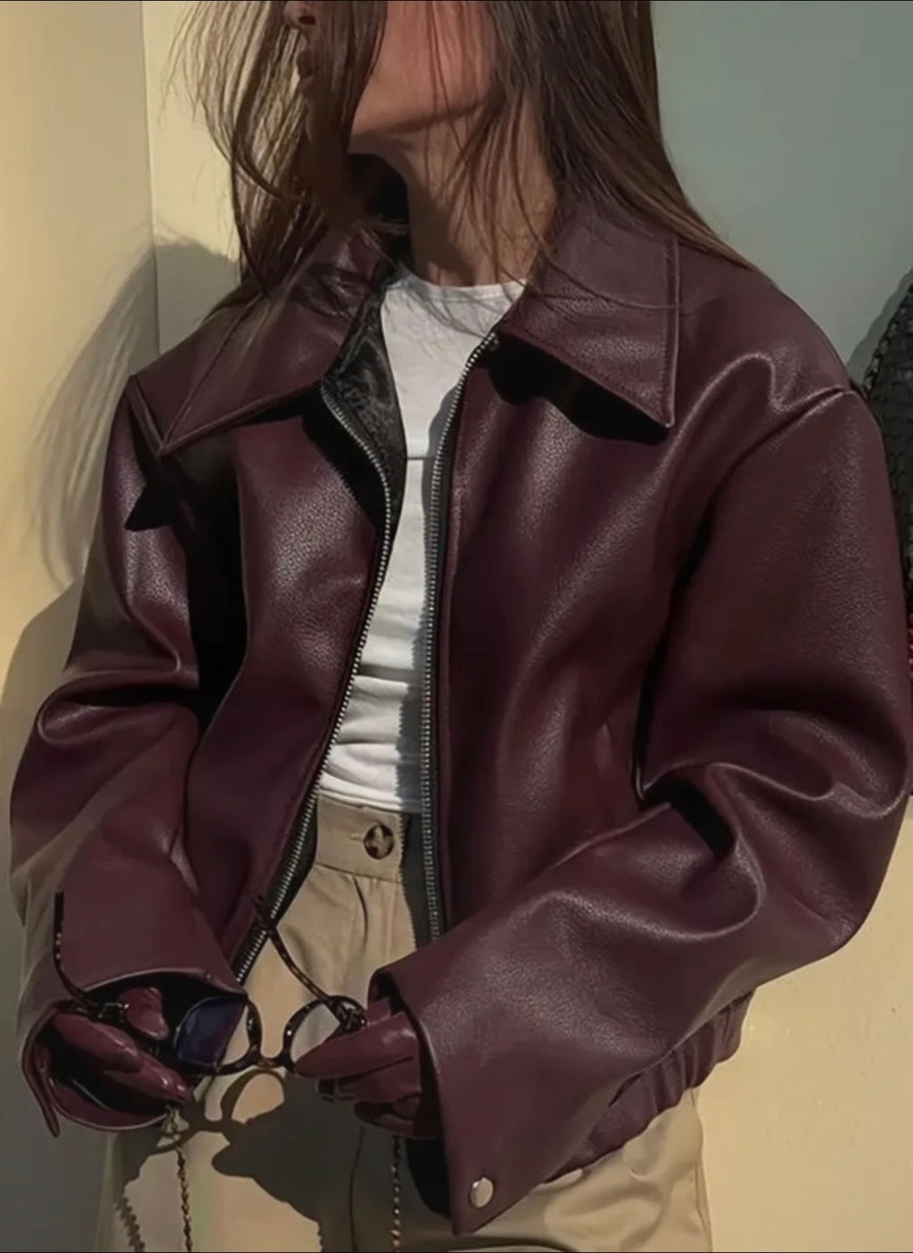 Person wearing a burgundy leather jacket with a neutral background
